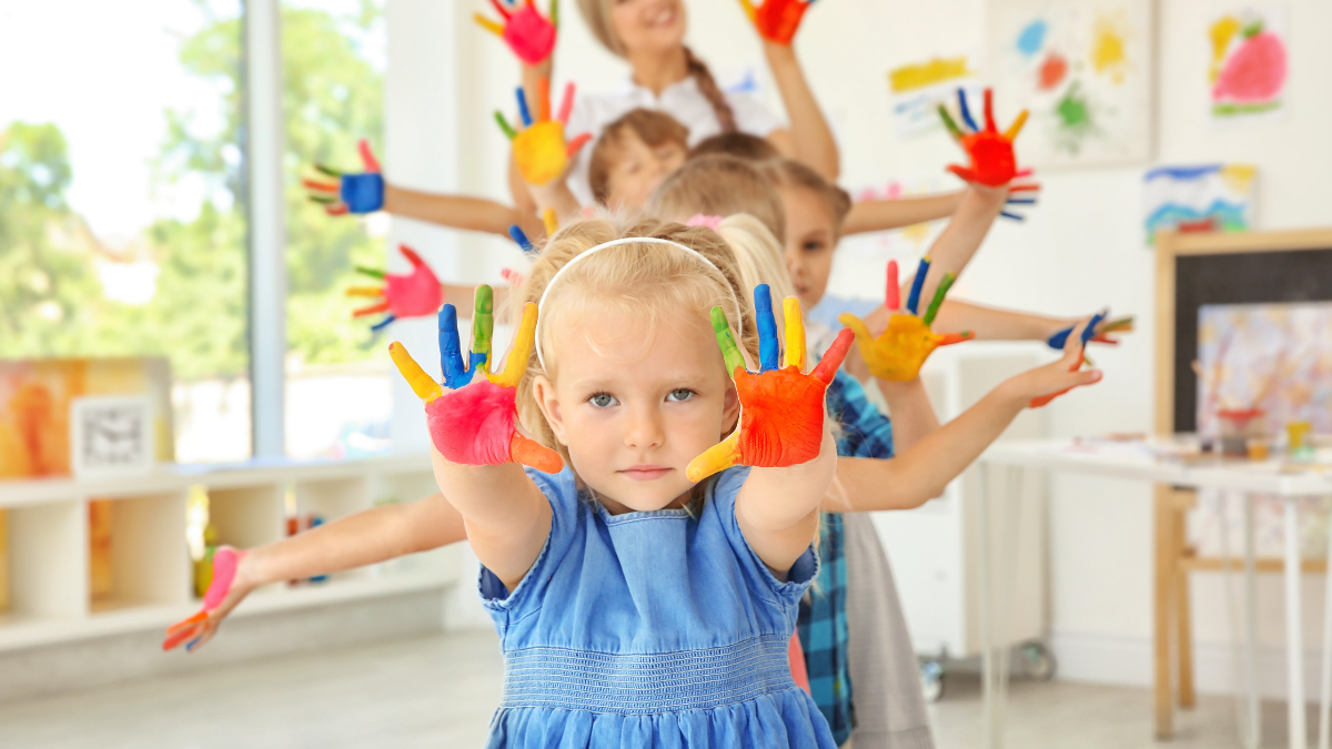 Imagen de un grupo de niños saludando con las manos pintadas